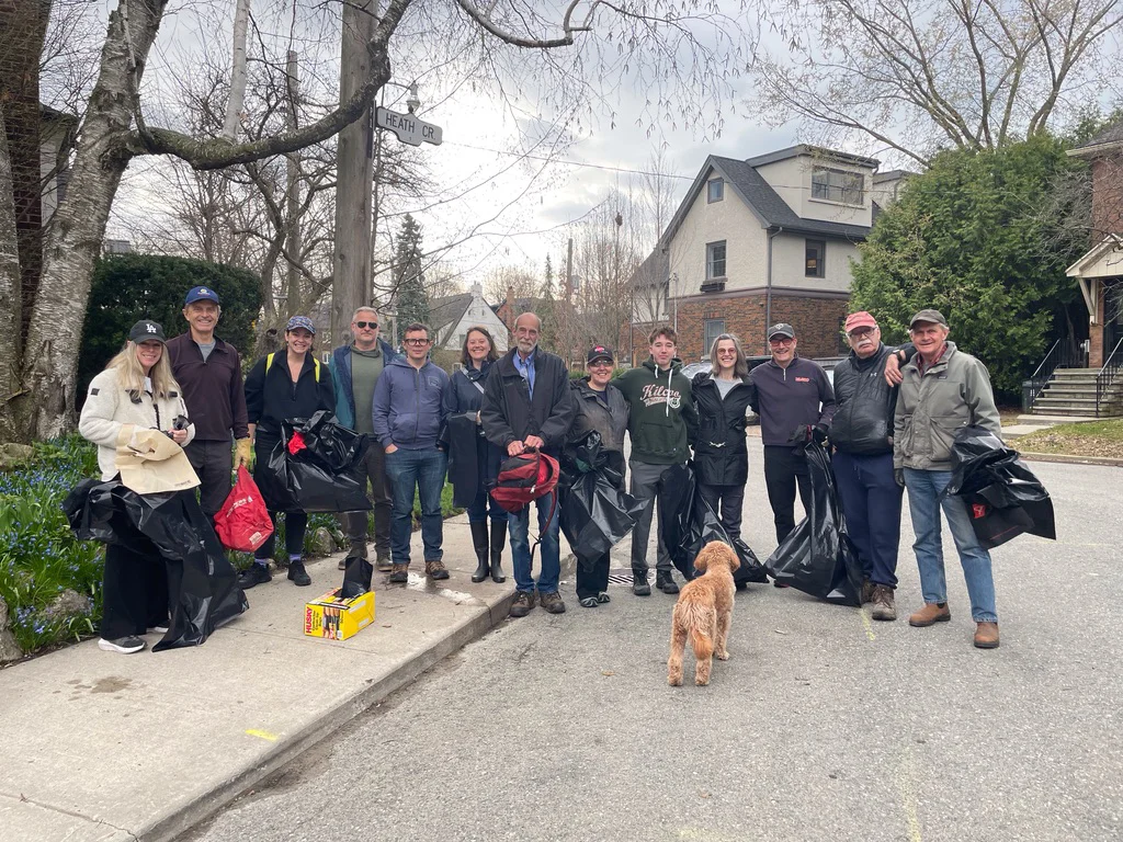 Group of adults and a dog standing on residential street holding garbage bags