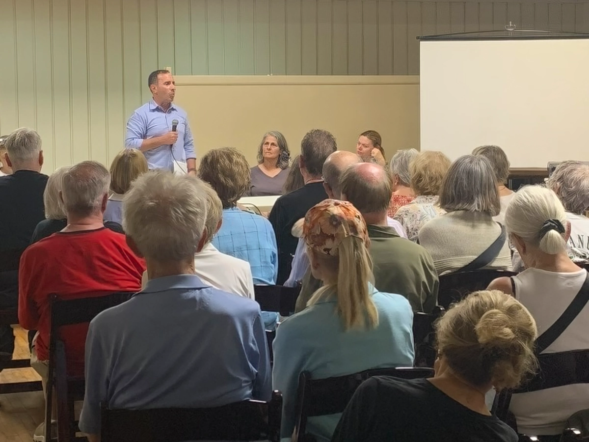 Man standing at front of meeting holding microphone in front of many seated adults