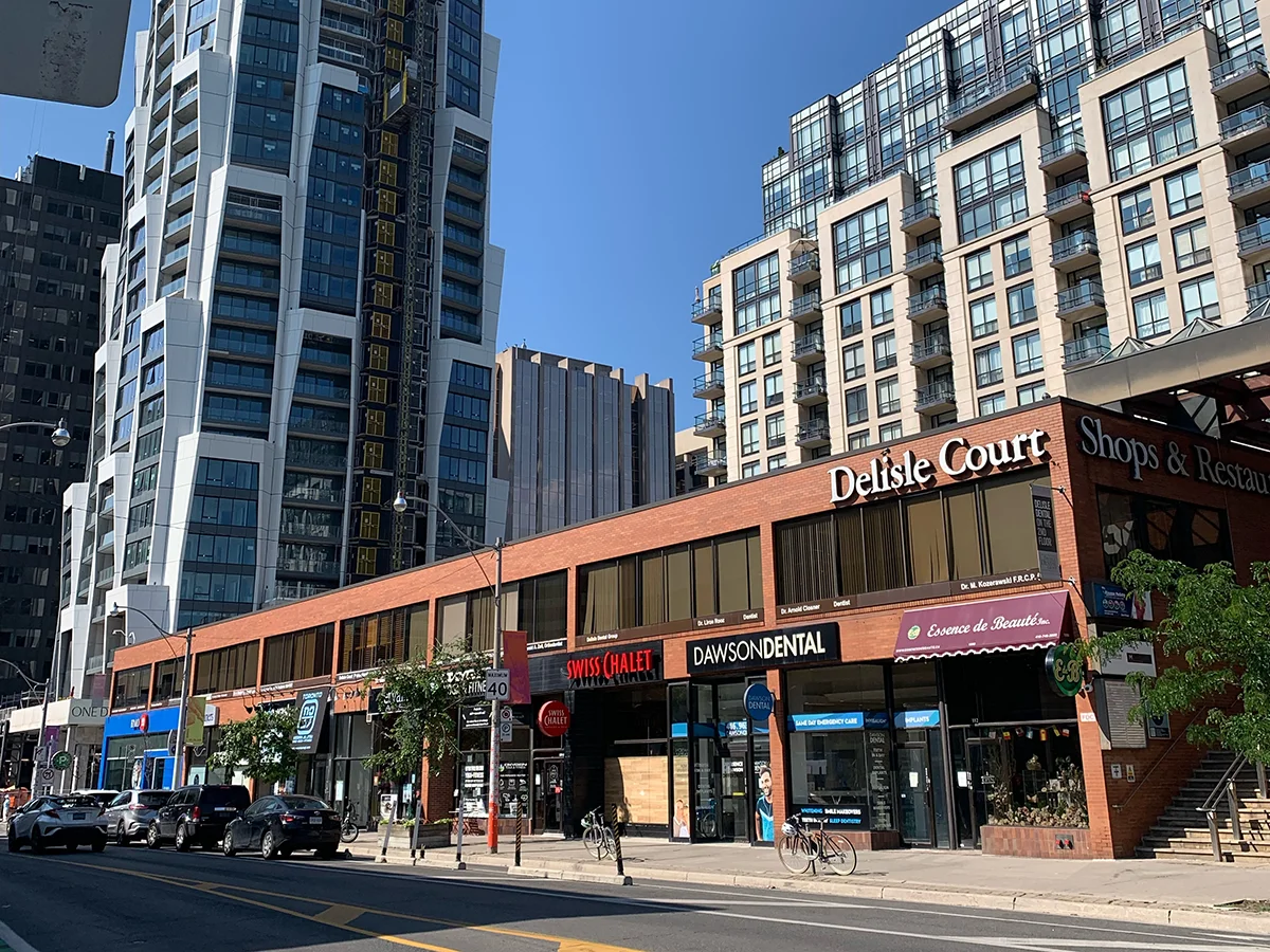 Low red brick building with shops at ground level with taller buildings behind.