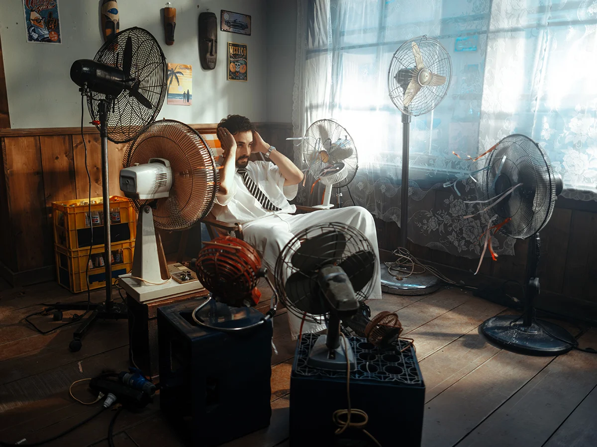 Distressed-looking man in chair surrounded by fans